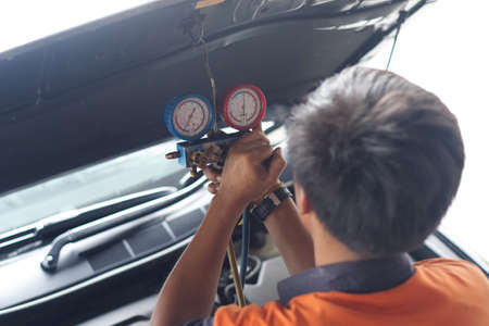 Asian mechanical worker are repairing the car by measuring refrigerant pressure in gauge hanging on...