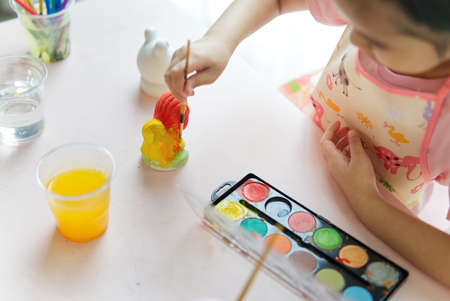 Close up shot of young little Asian girl painting animal plaster dolls in painting class at home. She holding paintbrush in the hand and painting the doll. Happy and fun creative activity concept.の写真素材