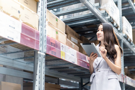 Smart smiling Asian woman works in storage warehouse. Girl stands and holding tablet computer and...