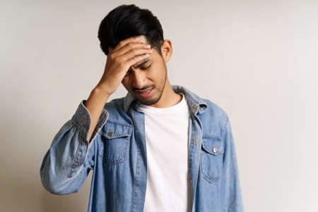 Young Asian man put hand to his head. He feeling sick and headache due to having some problems. His stress make him uncomfortable and unhappy. Seen on white background. Male expression concept.の写真素材