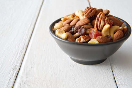 Mix nuts and dried fruits in the bowl put on the white painted wooden. Seen from side view. Food and snack concept.の写真素材