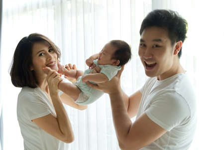Fun and play together. Asian family, father and mother are playing with their newborn baby. Dad...