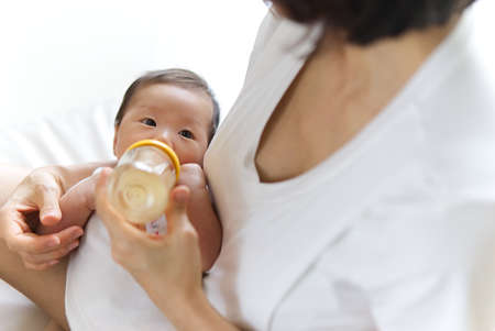 Close up view of Asian mother holding and feeding baby from milk bottle. Portrait of cute newborn...