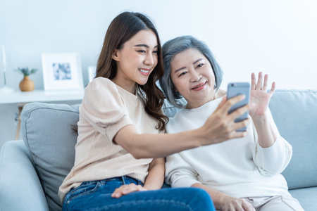 Asian happy family, senior mom use mobile phone with daughter at home. Attractive beautiful girl sit...