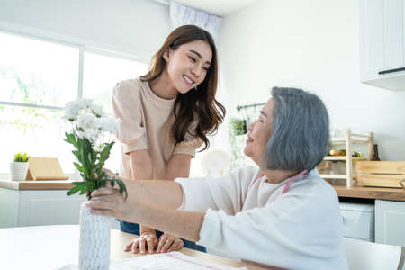 Asian active senior old woman puts flowers on vase with young daughter. Beautiful grandmother feel...