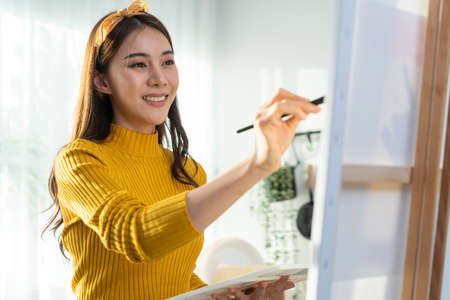 Asian young talented woman artist coloring on painting board in house. Attractive beautiful female draw art picture, creating artwork with watercolor paint and brush enjoy creativity activity at home.の写真素材