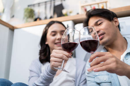 Asian young new marriage couple spend time together in kitchen at home. Attractive romantic man and woman sit of floor enjoy drink wine to celebrate family relationship life and moving to new house.の写真素材