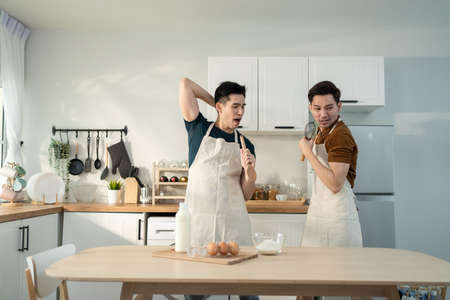 Asian happy handsome man gay couple sing and dance together in kitchen. Attractive romantic male...