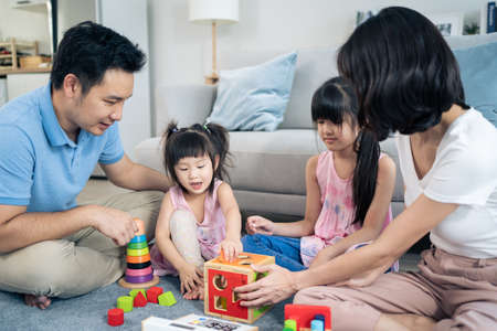 Asian happy family sit on floor, play kid toy together in living room. Attractive parents mother and...