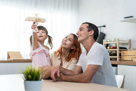 Asian attractive parents playing airplane toy with baby kid in kitchen. Happy family, young couple mother and father spend time on holiday together with daughter, prepare to cook foods for breakfast.の写真素材