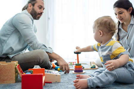 Caucasian happy loving parent play with baby toddler in living room. Attractive couple mother and father spend time with young little infant son child in house. Activity relationship at home concept.の写真素材
