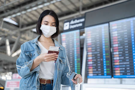 Caucasian woman passengers wear face mask walking in airport terminal. Young traveler girl standing...