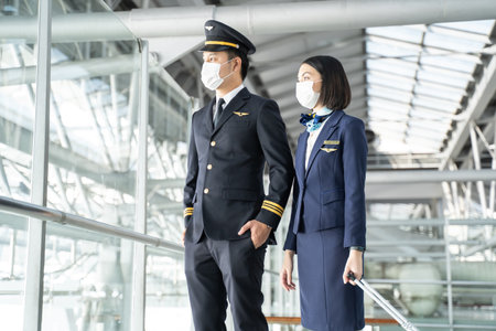 Commercial cabin crew or air hostess and pilot occupation concepts. Asian airliner pilot and air hostess wearing mask during pandemic walking and talking together in airport terminal to the airplane.の写真素材