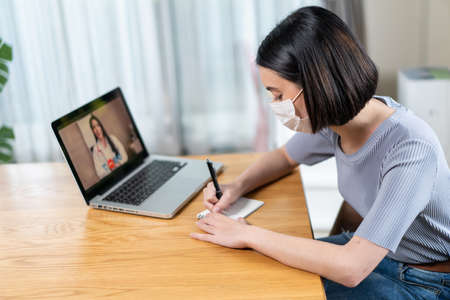 Asian young woman video call with doctor in living room at home. Patient girl consulting with general practitioner application computer laptop. Doctor and Consultant online and telemedicine concept.の写真素材