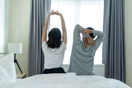 Rear view of Asian couple stretching hands after wakeup in morning. Attractive new marriage man and...
