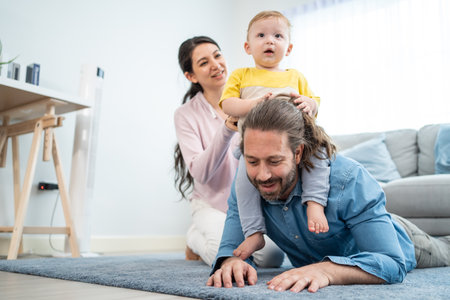 Caucasian happy loving parent play with baby toddler in living room. Attractive couple father carry young little infant son child on neck with mother on floor. Activity relationship at home in house.の写真素材