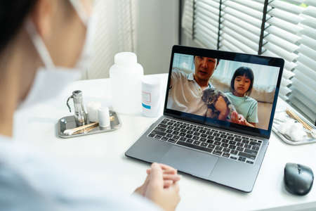 Asian veterinarian girl talk to pet owner on online virtual video call. Professional vet doctor woman use laptop computer to give treatment plan consult for little cat animal while sit in pet hospitalの写真素材