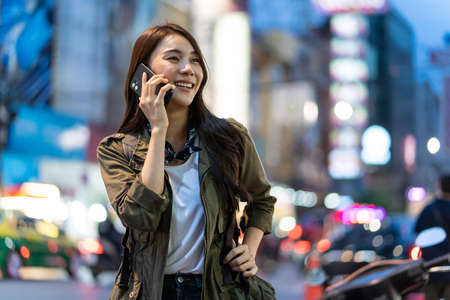 Asian attractive woman backpacker talking on mobile phone walk in city. Beautiful woman tourist traveler travel alone on street using smartphone enjoy spend time on holiday vacation trip at night roadの写真素材