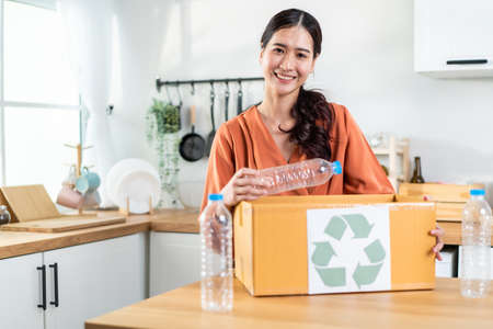 Portrait of Asian woman hold trash bin for further recycling at home. Attractive female put plastic...