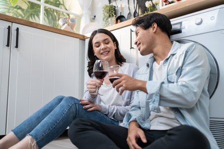 Asian young new marriage couple spend time together in kitchen at home. Attractive romantic man and woman sit of floor enjoy drink wine to celebrate family relationship life and moving to new house.の写真素材