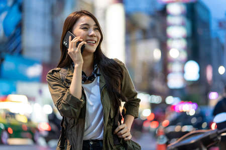 Asian attractive woman backpacker talking on mobile phone walk in city. Beautiful woman tourist traveler travel alone on street using smartphone enjoy spend time on holiday vacation trip at night roadの写真素材