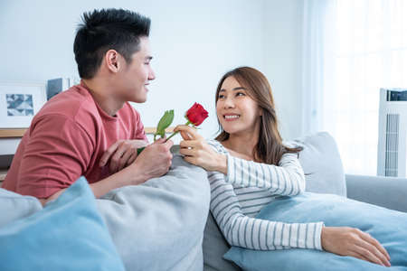 Asian young man surprise and give rose flower to beautiful girlfriend. Attractive romantic new...