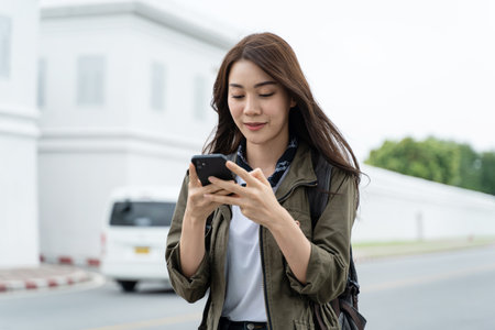 Asian attractive woman backpacker chatting on phone while walk in city. Beautiful woman tourist traveler travel alone on street using smartphone enjoy spend time on holiday vacation trip in Thailand.の写真素材