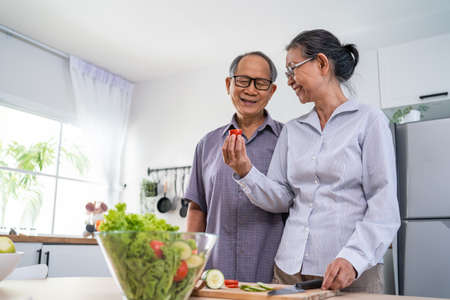 Asian loving senior elderly couple wear apron and cooking in kitchen. Attractive strong old man and...