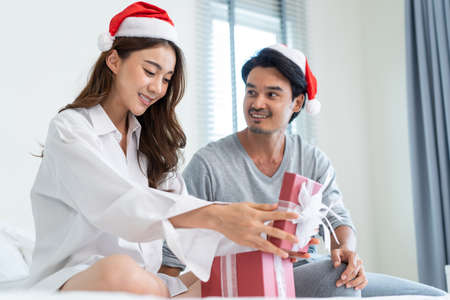 Asian beautiful young woman open xmas present gift box from boyfriend. Attractive girl feeling happy and excited for surprise from husband and ready to celebrate holiday Christmas together in house.の写真素材