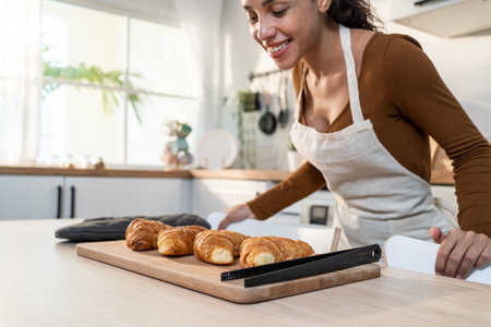Attractive young Latino woman baking croissant on table in kitchen. Beautiful female wear apron feel happy and enjoy spending leisure time cooking bakery at home. Activity homemade in house concept.の写真素材