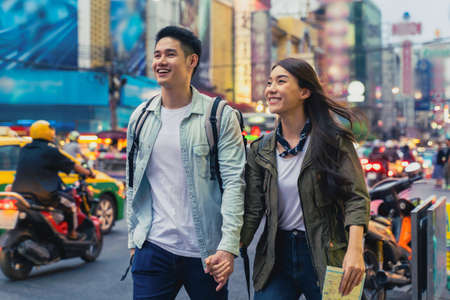 Asian active young couple travel in city for honeymoon trip at night. Attractive new marriage man and woman backpacker tourist walking on street enjoy spend time dating on valentines vacation togetherの写真素材