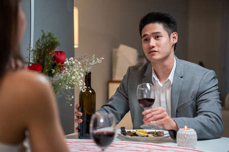 Asian young couple having dinner to celebrate valentine's day together. Attractive romantic new marriage man and woman having night party eat foods on table for wedding anniversary in kitchen at home.の写真素材