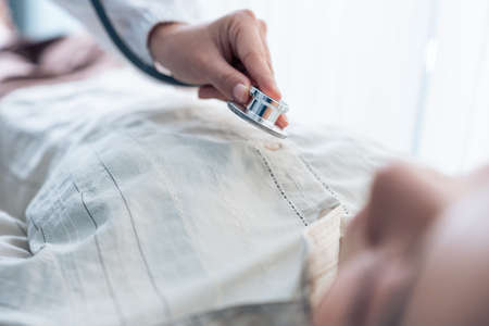 Close up hands of Asian physician doctor measure heart rate on patient. Attractive beautiful medical therapist female practitioner examiner young woman lying down on bed in recovery room in hospital.の写真素材