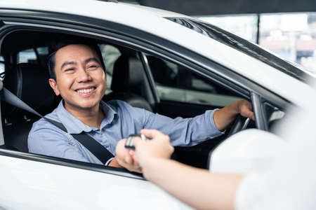 Asian automotive mechanic repairman handing car remote key to client. Vehicle service manager give...