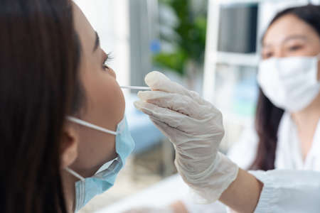 Young female physician use a rapid antigen test doing quick swab for patient during  pandemic in...