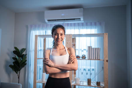 Portrait of Asian active young girl in sportswear stand crossing arms. Attractive beautiful women with six packs abs look at camera and smile after exercise or yoga, Spend time leisure in living room.