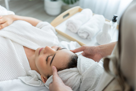 Asian young woman feel happy and relax during facial and head massage. Attractive beautiful girl lying on massage table, getting physiotherapy from masseuse for skin and body care in spa beauty salon.の写真素材