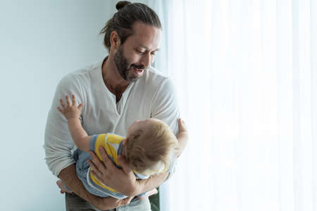 Caucasian loving father tosses cute baby boy child up in living room. Happy family, attractive...