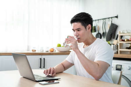 Asian business man drinking miniral water while sit working from home. Attractive handsome male feel...