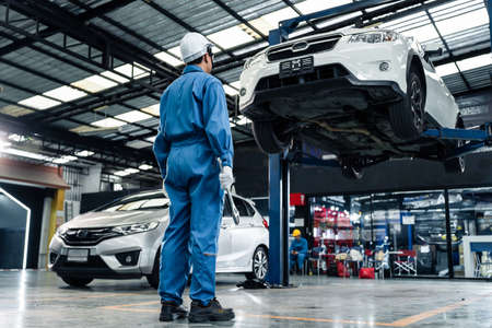 Rear view of Asian automotive mechanic repairman look under car condition in garage. Vehicle service...