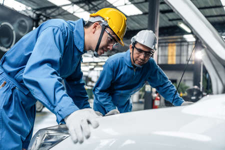 Asian two automotive mechanic men wear helmet work in mechanics garage. Team of vehicle service...