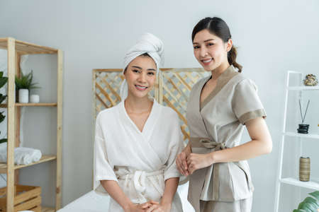 Portrait of Asian young masseuse woman and client looking at camera. Attractive beautiful girl sit...