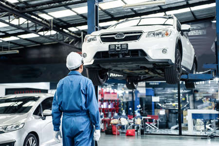 Rear view of Asian automotive mechanic repairman look under car condition in garage. Vehicle service...