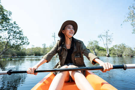 Asian young attractive tourist woman rowing kayak alone in forest lake. Backpacker traveler girl travelling and kayaking on canoe in beautiful mangrove forest enjoy spend time on holiday vacation tripcの写真素材