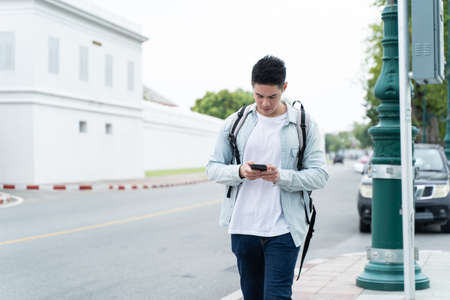 Asian attractive male backpacker chatting on mobile phone walk in city. Active handsome man tourist...