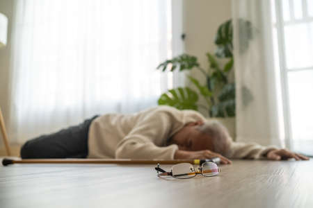 Asian senior male falling on the ground while walk with walker at home. Elderly older mature grandfather having an accident after doing physical therapy alone after retirement in living room in house.の写真素材