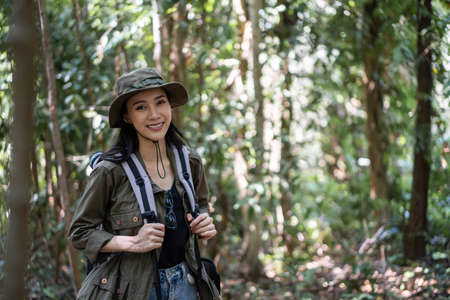 Portrait of Asian beautiful woman backpacker traveling alone in forest. Attractive girl traveler walk in nature wood with happiness and fun during holiday vacation trip then smiling, looking at cameraの写真素材