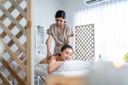 Asian young relaxing woman getting back massage therapy with hot stone. Attractive beautiful girl...