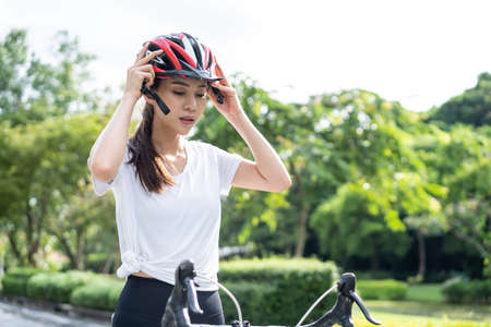 Asian young sport woman wearing helmet and prepare to riding bicycle. Beautiful athlete fit and firm girl in sportswear ready to exercise by cycling workout for health care in evening in public park.の写真素材