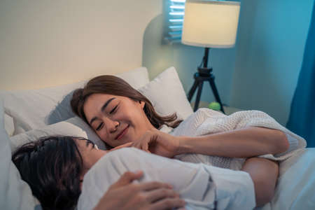 Asian beautiful lesbian couple lying down on bed and hugging each other. Attractive romantic girl friend in pajamas spending night leisure time together in bedroom in houseの写真素材